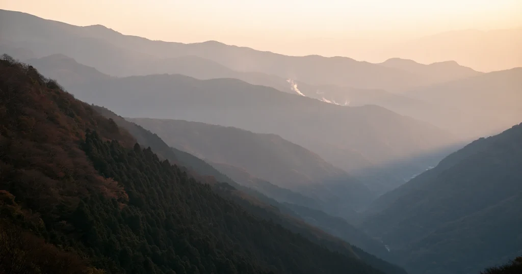 Layered Japanese mountain valleys in soft morning light, evoking the quiet approach to an onsen ryokan.