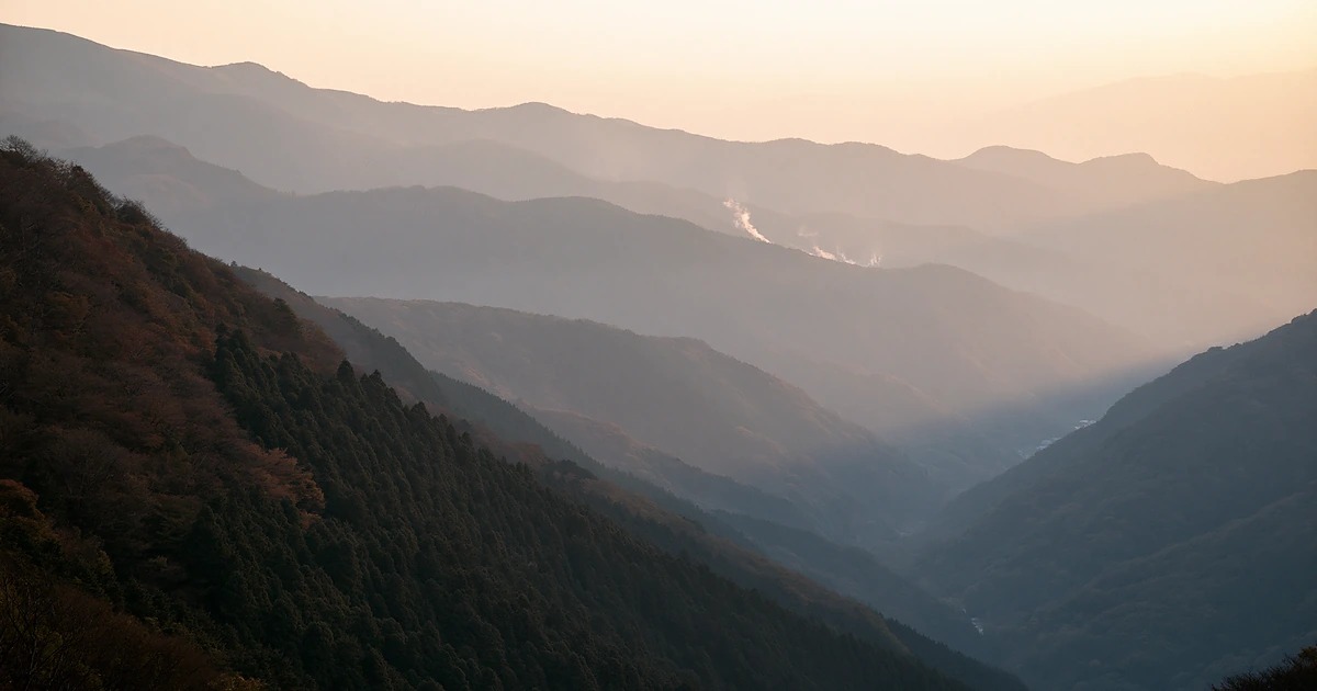 Layered Japanese mountain valleys in soft morning light, evoking the quiet approach to an onsen ryokan.